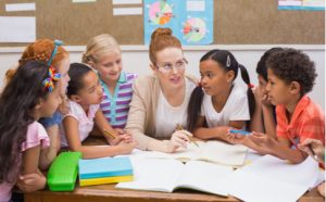 Lehrerin sitzt mit ihren Schülern am Tisch und erklärt etwas
